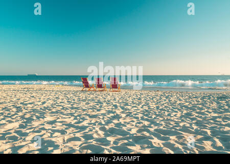 Tramonto sulla spiaggia. Vuoto bella spiaggia di sabbia e tre sedie a sdraio sulla spiaggia Foto Stock