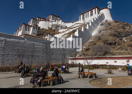 Pellegrini tibetani riposo dal loro circumambulation al di sotto del palazzo del Potala a Lhasa, in Tibet. Un sito Patrimonio Mondiale dell'UNESCO. Foto Stock