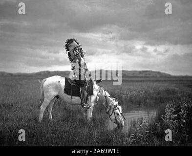 Edward S. Curtis nativi indiani americani - Rosso Hawk, un guerriero Oglala, seduto su un cavallo che è di bere da un piccolo stagno nel Badlands ca. 1905 Foto Stock