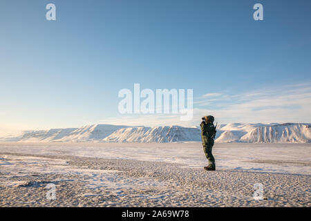 Uomo con un fucile e binocoli guardando fuori sul paesaggio artico a Svalbard Foto Stock
