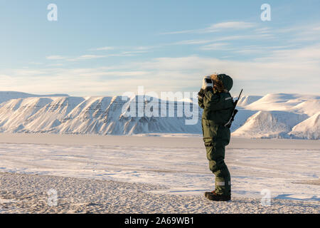 L'uomo nel paesaggio artico. Persona in piedi con un fucile e binocoli, guardando il paesaggio artico a Svalbard Foto Stock