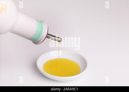 Versando l'olio di oliva in un piccolo piatto bianco isolato sopra sfondo bianco con spazio per la copia Foto Stock