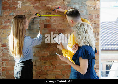 Interior designer che lavora con coppia giovane. Famiglia deliziosa e designer professionista o architector conept discutendo del futuro interno, lavorando con tavolozza di colori e disegni in camera in un ufficio moderno. Foto Stock