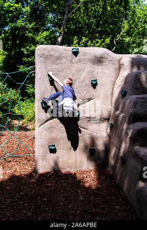 Un simpatico atletico ragazzino con ADHD, autismo, sindrome di Aspergers pratica con la sua abilità di arrampicata su una piccola parete di arrampicata in Colchester Country Park Foto Stock