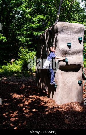 Un simpatico atletico ragazzino con ADHD, autismo, sindrome di Aspergers pratica con la sua abilità di arrampicata su una piccola parete di arrampicata in Colchester Country Park Foto Stock