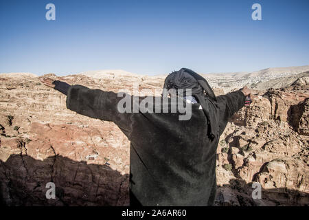 Bedouin uomo che indossa un nero abiti tradizionali e la copertura della testa oltre la vista incredibile di Petra national park in Giordania Foto Stock