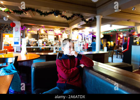 Un bel po' di ragazzo con ADHD, autismo, sindrome di apserger si siede in un ristorante, un pub in attesa di guardare la televisione a Yates a Newcastle under Lyme Foto Stock