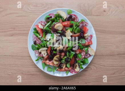Fresco e salutare la deliziosa insalata mista : verde mache, pomodori, parmigiano, aceto balsamico, salsiccia secca, mirtilli rossi & crostini. Un tavolo di legno. Foto Stock