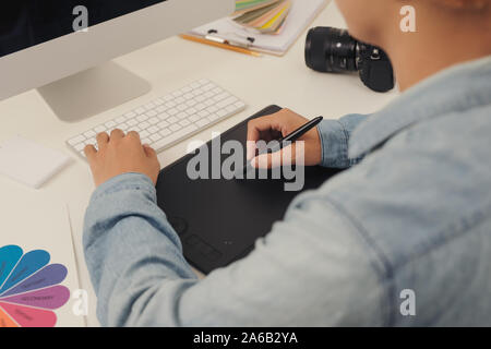 Fotografo il disegno e il ritocco immagine sul computer portatile, utilizzando una tavoletta digitale e penna stilo. Primo piano della mano d'uomo con fotocamera DSLR in backgro Foto Stock