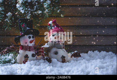 Scena notturna di due pupazzi di neve vacanze figurine con caduta di neve su un rustico in legno con sfondo spazio copia Foto Stock