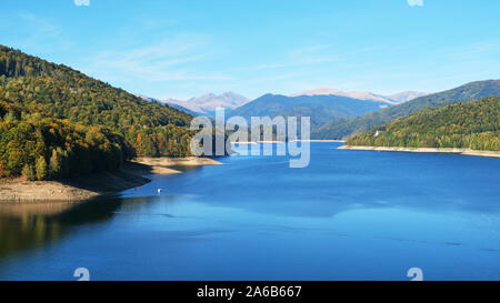 Il lago di Vidraru visto dalla diga di Vidraru, Arges county, Romania, con Fagaras picchi di montagna nella distanza, su una chiara e soleggiata giornata autunnale. Foto Stock