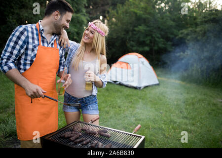 Coppia giovane con amici sorrisi e fare barbecue arrosto in campeggio Foto Stock