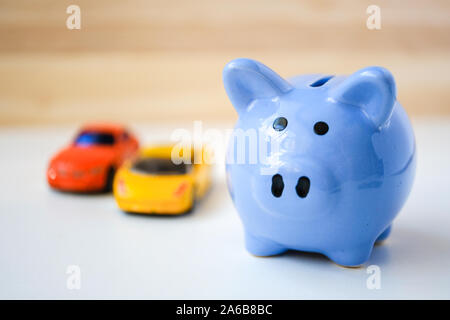 Close up di blu salvadanaio e due automobili giocattolo su bianco e lo sfondo di legno. Foto Stock