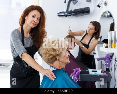 Parrucchiere professionista preparazione senior donna cliente per lo styling dei capelli, dressing parrucchieri cape Foto Stock