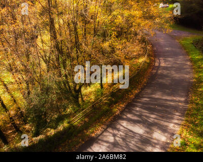 Viste autunnali dal suolo e antenna di foglie d'oro lungo un percorso a piedi e una strada di piegatura oltre il ponte in montagna Foto Stock