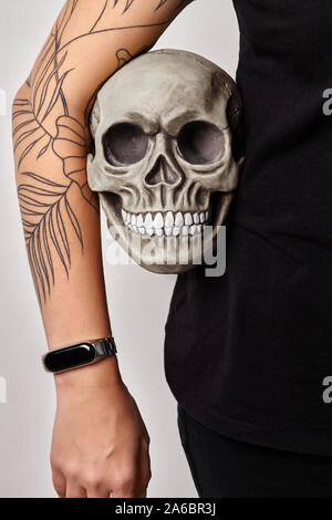Tatuato mani di una donna in una black Watch e vestiti è in possesso di un modello realistico di un teschio umano con denti sotto il suo braccio, isolato su bianco. Medic Foto Stock