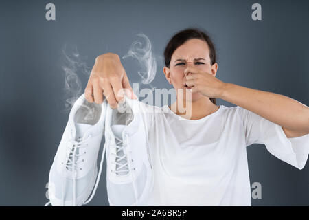 Close-up di una donna che copre il suo naso tenendo Stinky scarpe su sfondo grigio Foto Stock