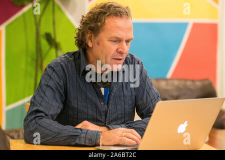 Un uomo si siede a un tavolo in una sala colorata al lavoro su un notebook Foto Stock