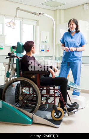 Un infermiere dentali parla di un paziente disabile in uno specialista su sedia a rotelle Sedia dentale Foto Stock