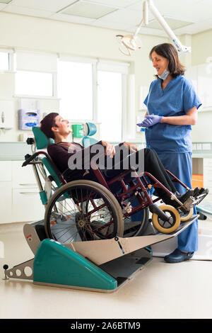 Un infermiere dentali parla di un paziente disabile in uno specialista su sedia a rotelle Sedia dentale Foto Stock