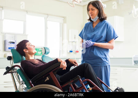 Un infermiere dentali parla di un paziente disabile in uno specialista su sedia a rotelle Sedia dentale Foto Stock