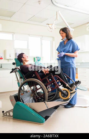 Un infermiere dentali parla di un paziente disabile in uno specialista su sedia a rotelle Sedia dentale Foto Stock