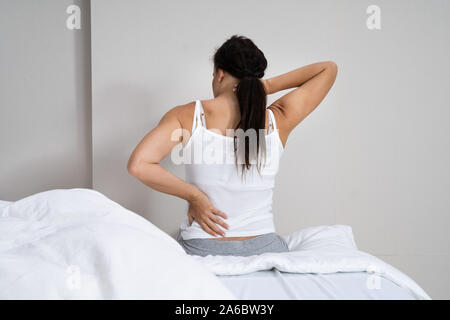 La donna che soffre di dolori alla schiena seduta sul letto Foto Stock