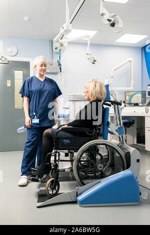 Un infermiere dentali parla di un paziente disabile in uno specialista su sedia a rotelle Sedia dentale Foto Stock