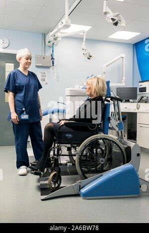 Un infermiere dentali parla di un paziente disabile in uno specialista su sedia a rotelle Sedia dentale Foto Stock