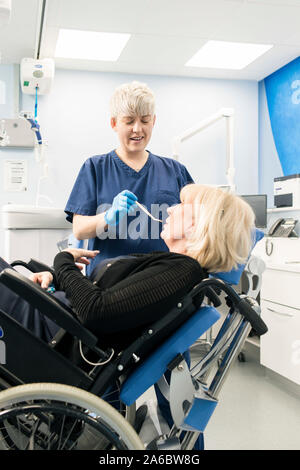 Un infermiere dentali parla di un paziente disabile in uno specialista su sedia a rotelle Sedia dentale Foto Stock