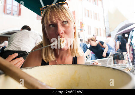 Una donna si siede al di fuori di un bar / ristorante in Francia e mangia la fonduta di formaggio fuso. Foto Stock