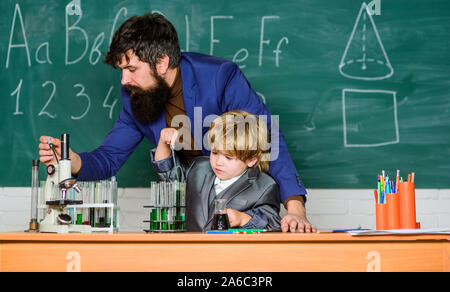 Insegnante uomo con little boy. La scuola le attrezzature di laboratorio. studente facendo esperimenti scientifici con microscopio in laboratorio. Si torna a scuola. il padre e il figlio a scuola. usando microscopio in laboratorio. Vivere in epoca digitale. Foto Stock