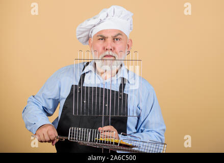 Egli preferisce il cibo alla griglia. Per picnic e barbecue. Regole di cucina. preparare la cena per la famiglia. Week-end in famiglia. senior uomo in chef hat. cuocere gli uomini con la barba. utensili di cottura per barbecue. Foto Stock