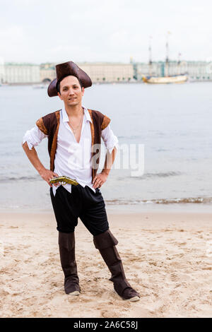 Uomo in costume pirata mettere le mani sui suoi fianchi sulla spiaggia sabbiosa. Verticale. Foto Stock