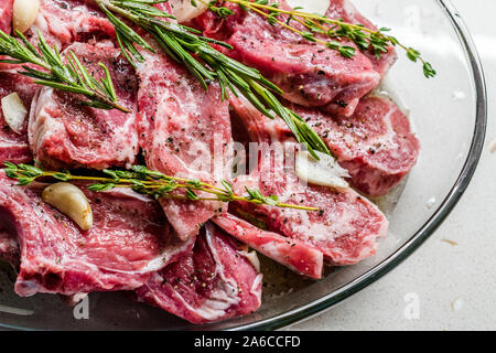 Materie marinata di costolette di agnello con rosmarino, olio d'oliva e aglio in recipiente di vetro. Pronto per cucinare e mangiare. Foto Stock