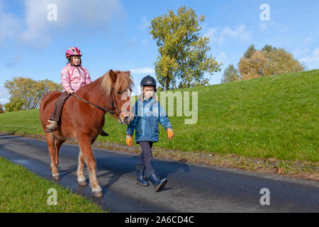 Una bambina a cavallo di un pony che è guidato da un'altra ragazza. Foto Stock