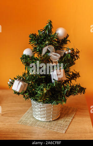 Miniatura albero di Natale sul tavolo vicino a Orange parete. Foto Stock