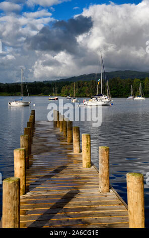 Luce del sole di mattina sul molo di legno che conducono a ormeggiate barche a vela sul lago di Windermere a Waterhead Ambleside Cumbria Inghilterra England Foto Stock