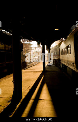 Drammatico pomeriggio luce alla Hoboken terminal del treno. Luce posteriore di creare forti ombre su tutta la piattaforma, treno e tracce. Colore verticale photog Foto Stock