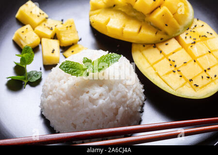 Close-up di Thai dessert cremoso, riso cotto con il latte di cocco e servita con mango fresco su una piastra nera su una tavola di legno Foto Stock