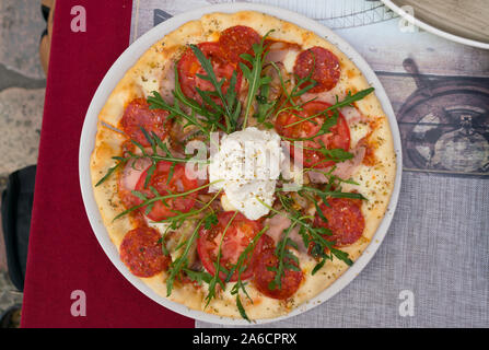 Pizza con salame, pomodori e rucola su una piastra Foto Stock