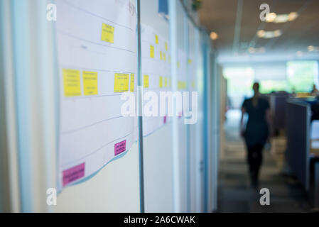 Un membro del personale cammina verso il basso un piano aperto ufficio corridoio in un ufficio moderno Foto Stock