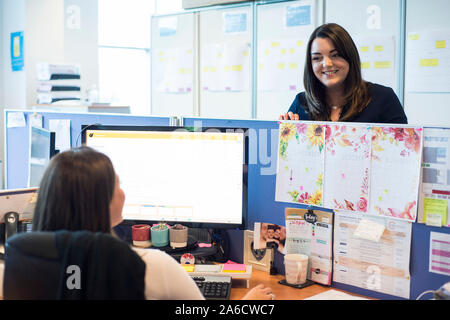 Due elementi femmina di chat personale attraverso un ufficio open space al di sopra dei divisori Foto Stock