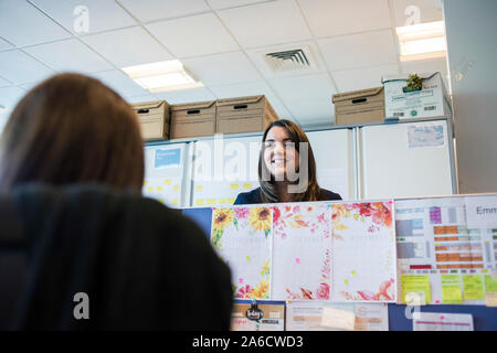 Due elementi femmina di chat personale attraverso un ufficio open space al di sopra dei divisori Foto Stock