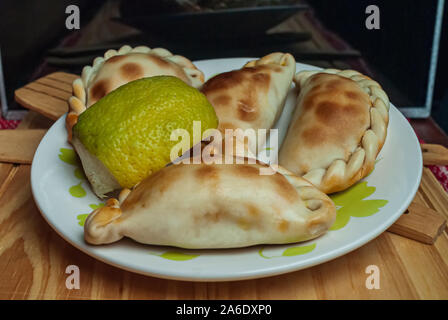 In casa le empanadas (dettagliate di close-up shot; messa a fuoco selettiva) tipico della campagna Argentina gastronomia, sulla piastra bianca su tavola in legno rustico. Foto Stock