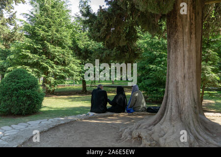 TBILISI, GEORGIA - luglio 6, 2019: un sacerdote e una donna a sedersi su una panchina di conversazione nell'ombra di un albero in early morning sun. Foto Stock