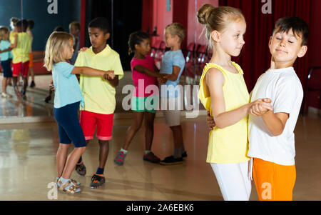 Sorridere i bambini della scuola primaria di ballo cercando partner di ballo in studio moderno Foto Stock