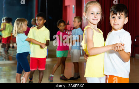 Il gruppo di allegro sorridente cercando per bambini danza con partner in aula Foto Stock