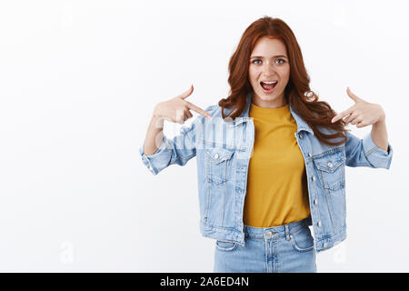 Orgogliosa e sassy bella redhead donna in camicia di denim, sorridente arrogante, indicando se stessa come la vanteria, magniloquente permanente che raccontano proprio Foto Stock