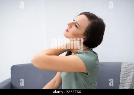 Donna con dolore al collo seduti a casa Foto Stock